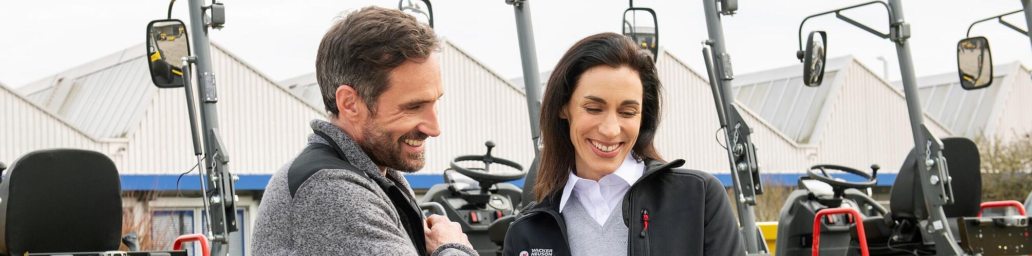 威克诺森员工面带微笑，使用平板电脑在威克诺森建筑机械前为微笑着的客户提供建议。